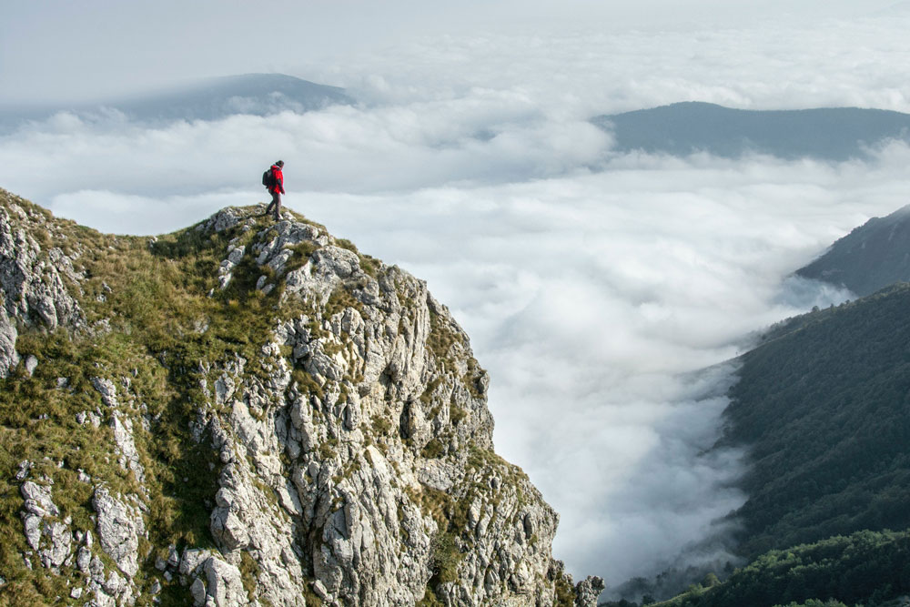 hiking man overlooks a cloudy mountain valley