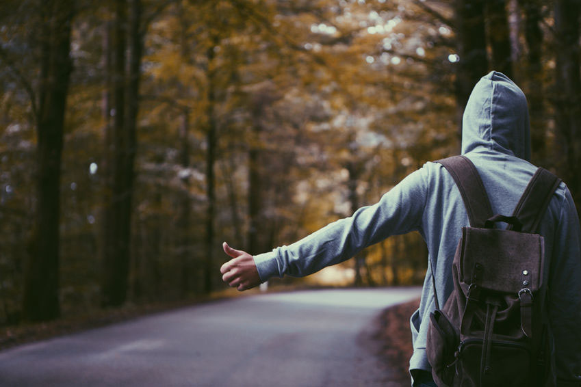 man in hoodie hitchhiking on a rural road