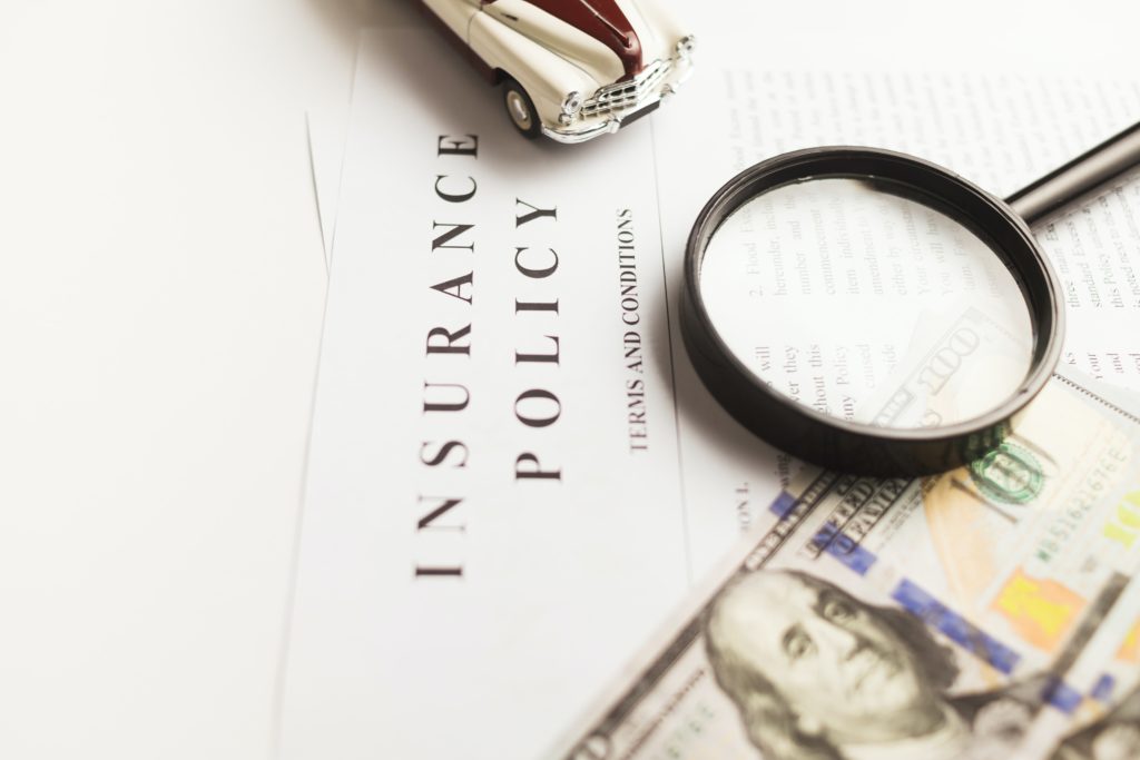 insurance policy terms and conditions with a toy car, magnifying glass, and money